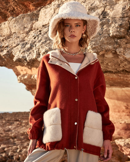 Woman wearing a red coat with white fur trim and a white hat in a rocky outdoor setting