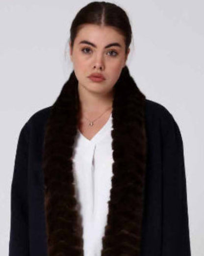 Woman wearing a long dark alpaca overcoat with a mink fur-lined hood on a white background