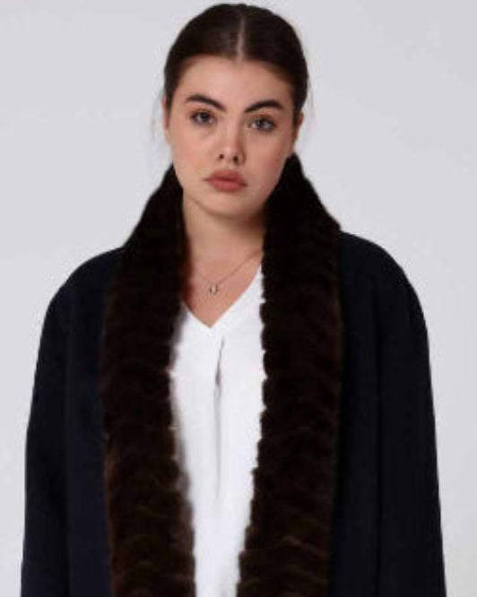 Woman wearing a long dark alpaca overcoat with a mink fur-lined hood on a white background