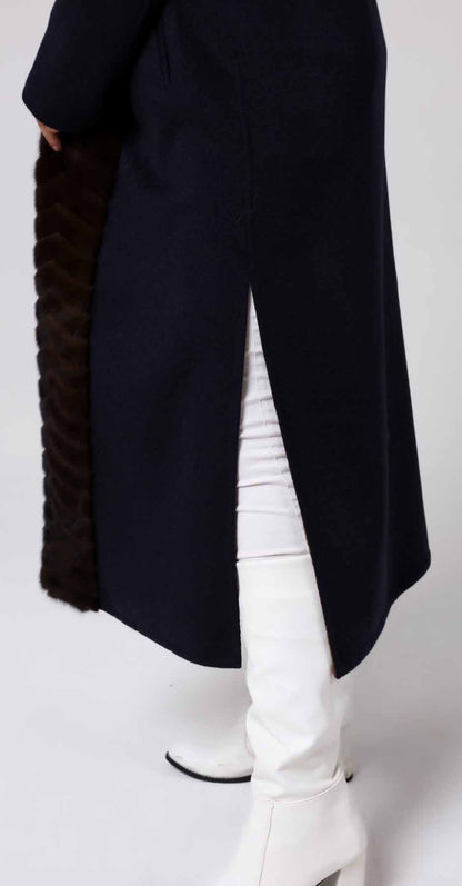 Woman wearing a long black alpaca  overcoat with a textured sleeve, white pants, and white boots on a white background