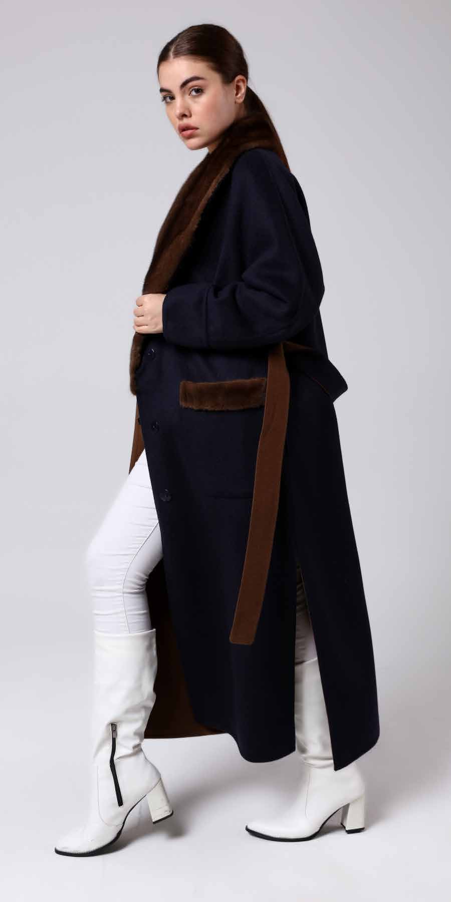 Woman wearing a alpaca overcoat with a mink fur and brown belt, white pants on a light gray background