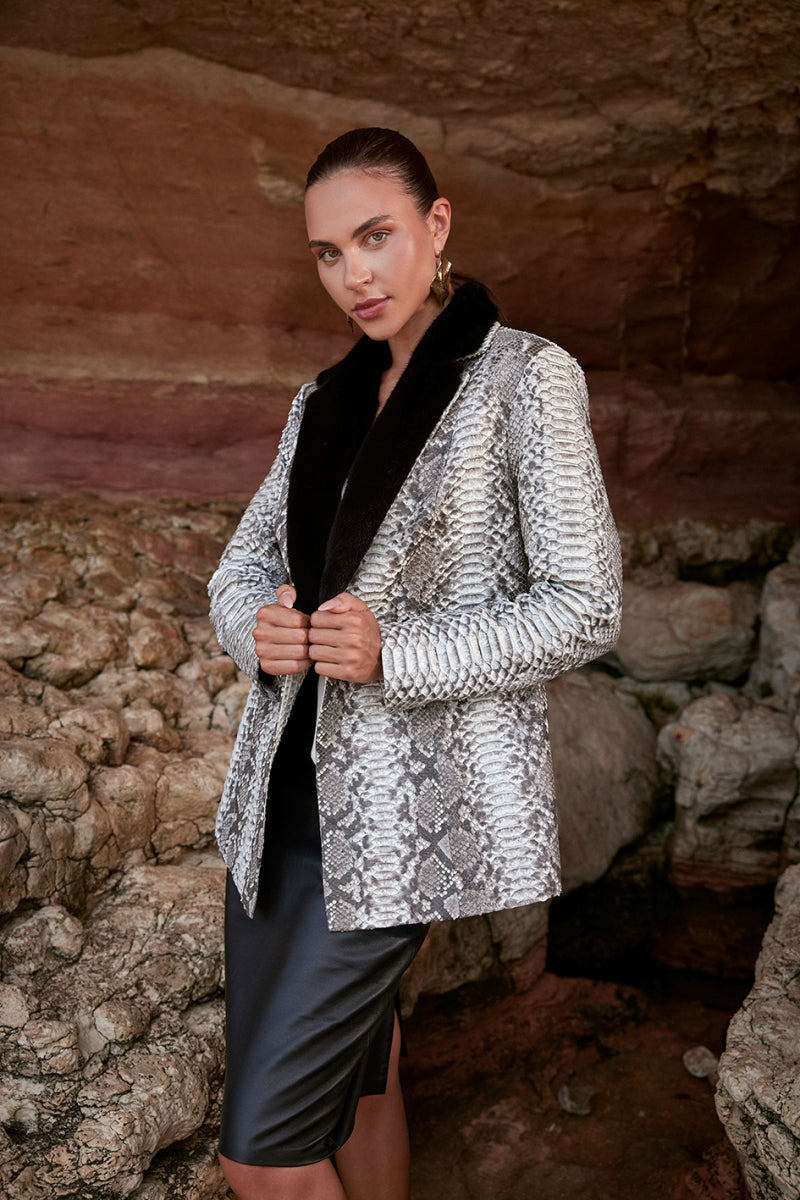 Woman wearing a silver snake print jacket in front of a stone wall.