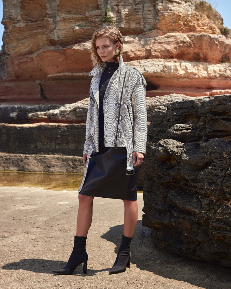 Woman standing in front of rock formations wearing a patterned cardigan and black skirt.