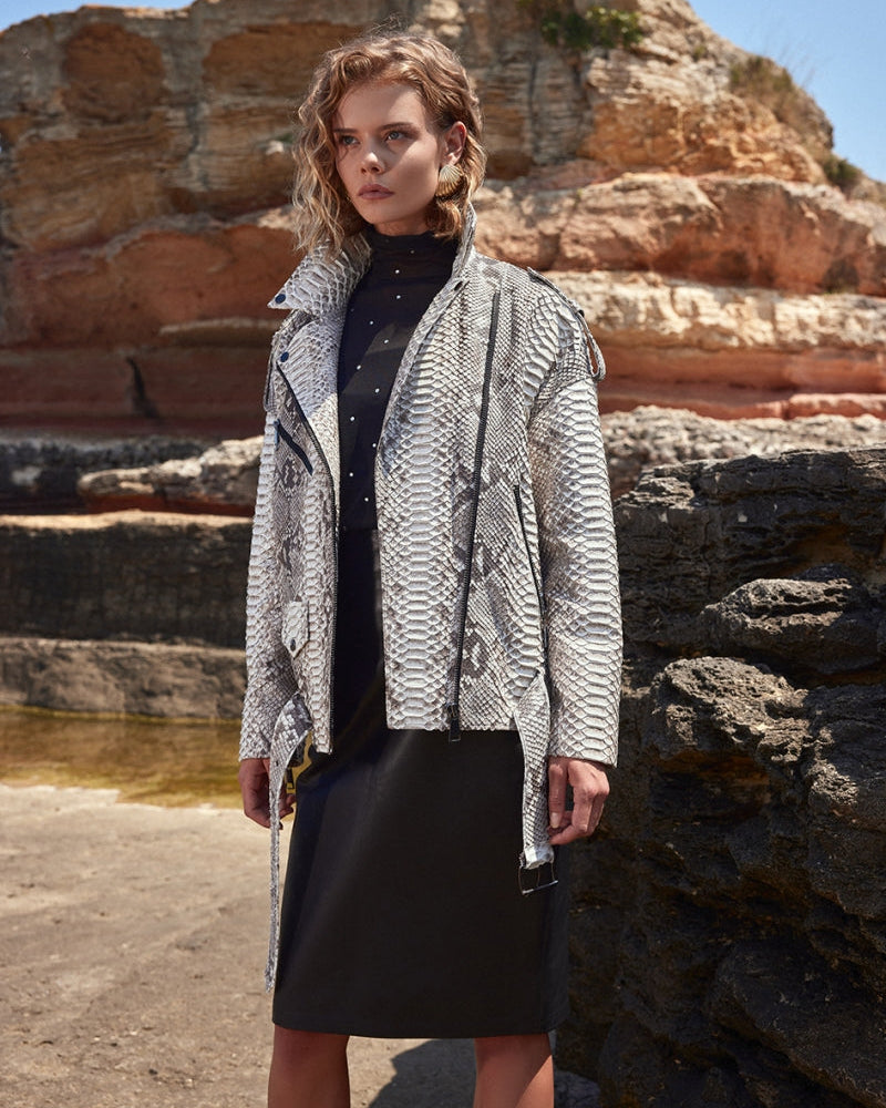 Woman wearing a patterned coat standing in front of rocky cliffs.