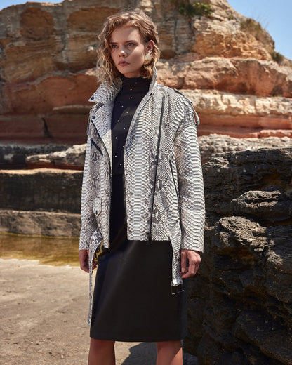Woman wearing a patterned coat standing in front of rocky cliffs.