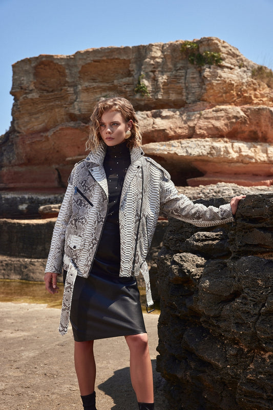 Woman standing in front of a rocky landscape wearing a patterned coat.
