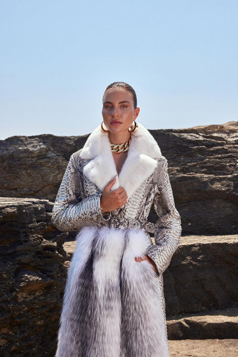 Woman wearing a stylish outfit with a fur coat and patterned jacket against a rocky background.