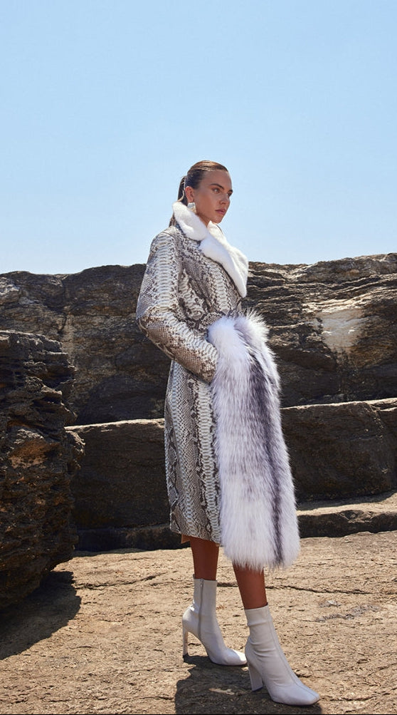 Woman wearing a fur coat standing on rocky terrain with clear blue sky