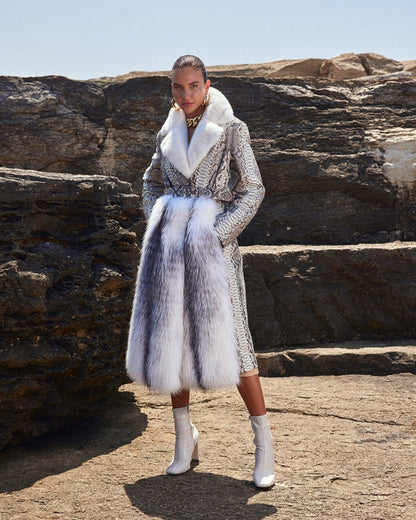 Woman wearing a stylish outfit with a fur coat and patterned dress against a rocky background.