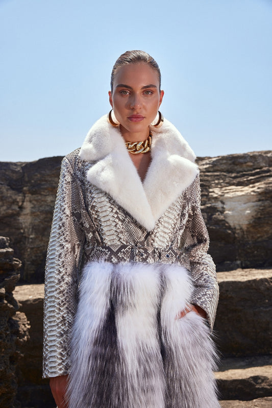 Woman wearing a stylish outfit with a fur-trimmed coat and scarf against a natural background.