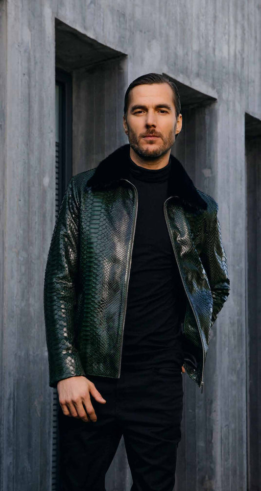 Man wearing a dark green leather jacket over a black shirt against a gray concrete wall.
