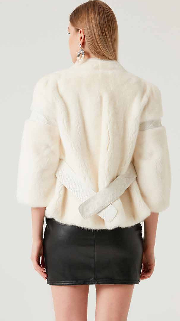 Person wearing a white jacket, black leather skirt, and black knee-high boots on a plain background