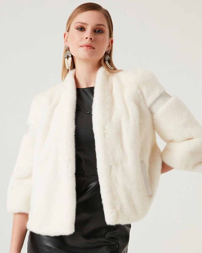 Woman wearing a white fur vest over a black dress on a plain background