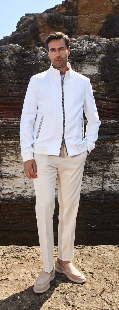 Man in a white jacket and beige pants standing against a rocky background