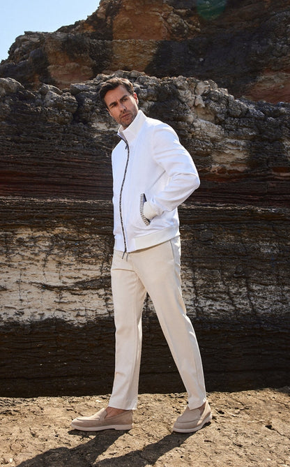 Man in a white jacket and beige pants standing against a rocky background