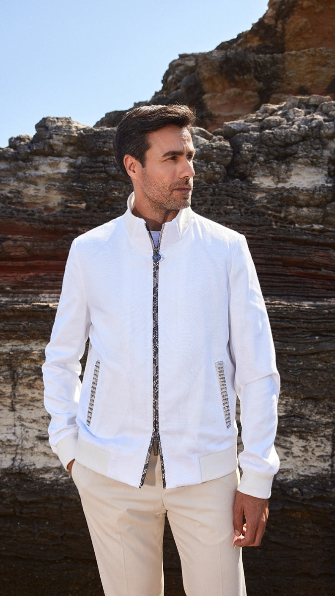 Man wearing a white jacket and beige pants standing against a rocky background