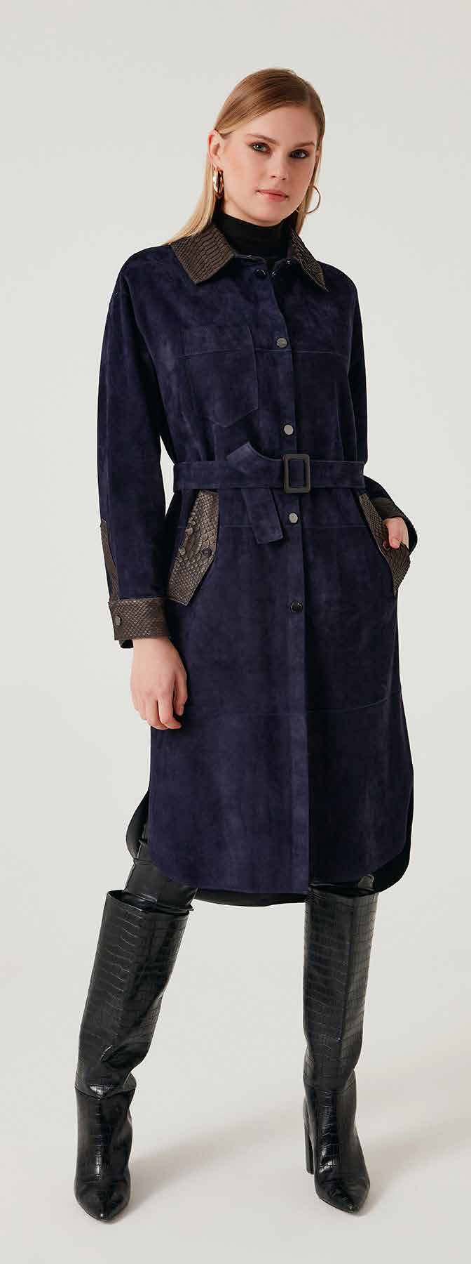 Woman wearing a long navy coat with leather accents on a white background