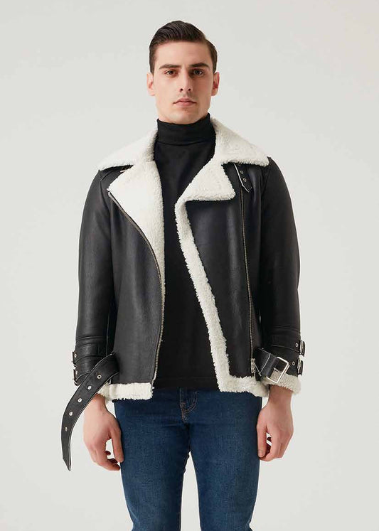 Man wearing a black leather jacket with white shearling lining, black turtleneck, blue jeans, and black boots on a white background.