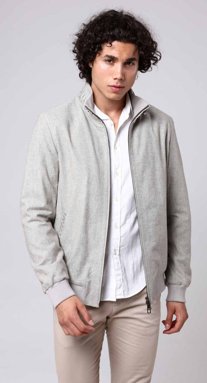 Man wearing a light gray jacket over a white shirt and beige pants on a plain background