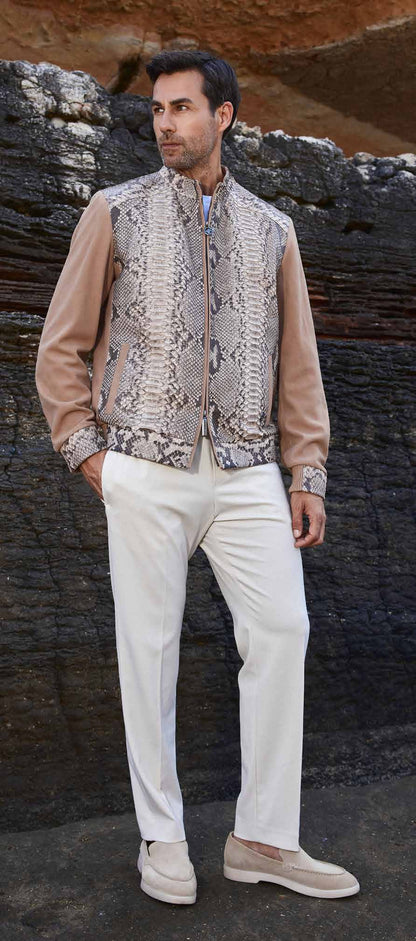 Man wearing a patterned vest over a beige shirt with white pants against a rocky background
