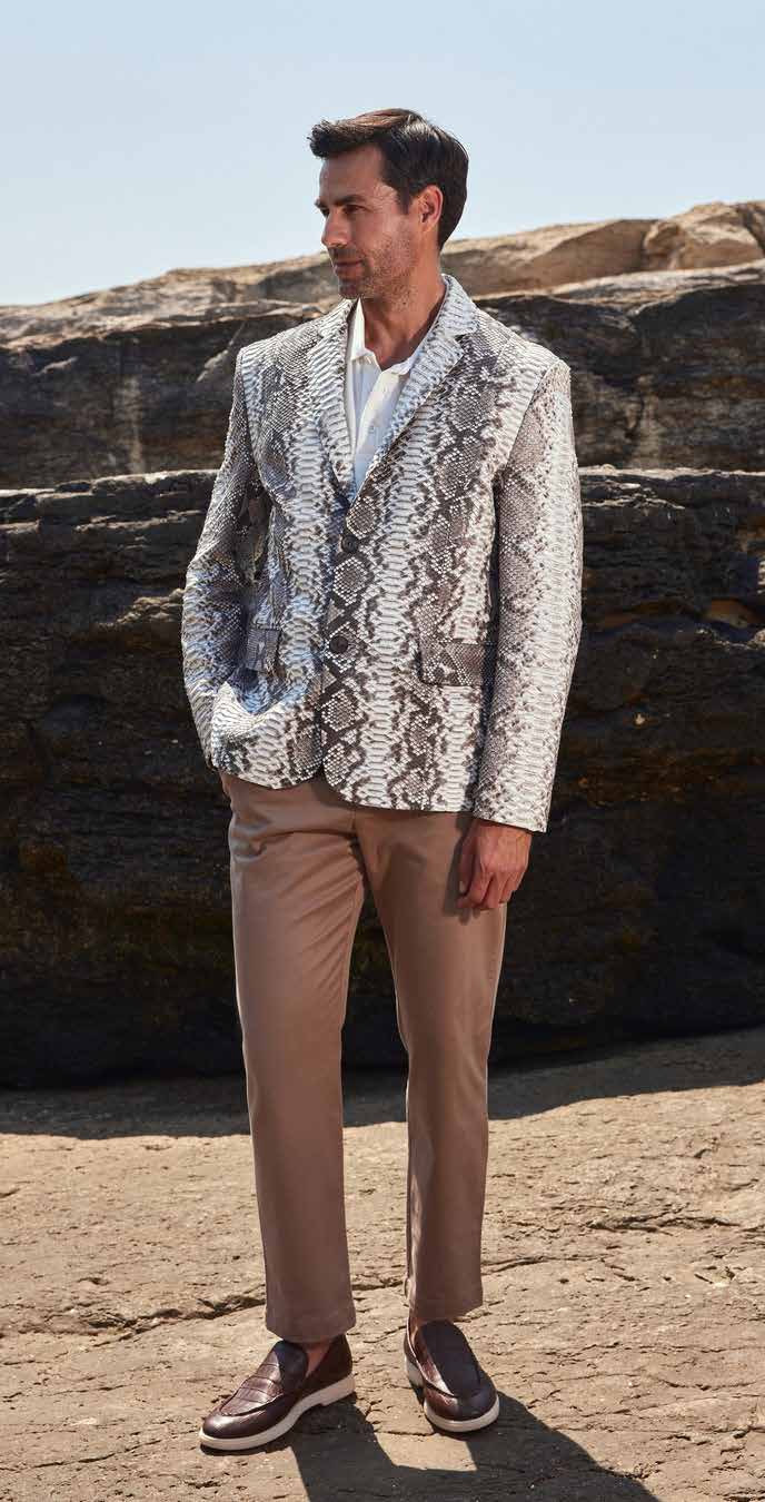 Man wearing a patterned blazer and beige pants standing against a rocky background
