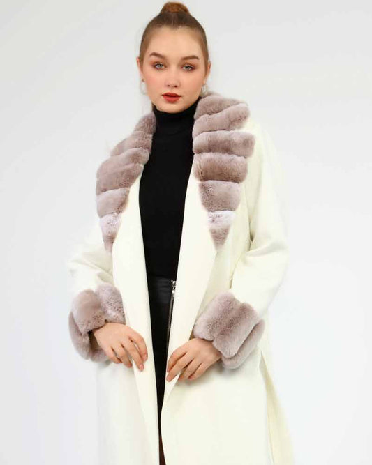 Woman wearing a long cream coat with rex fur trim on a white background