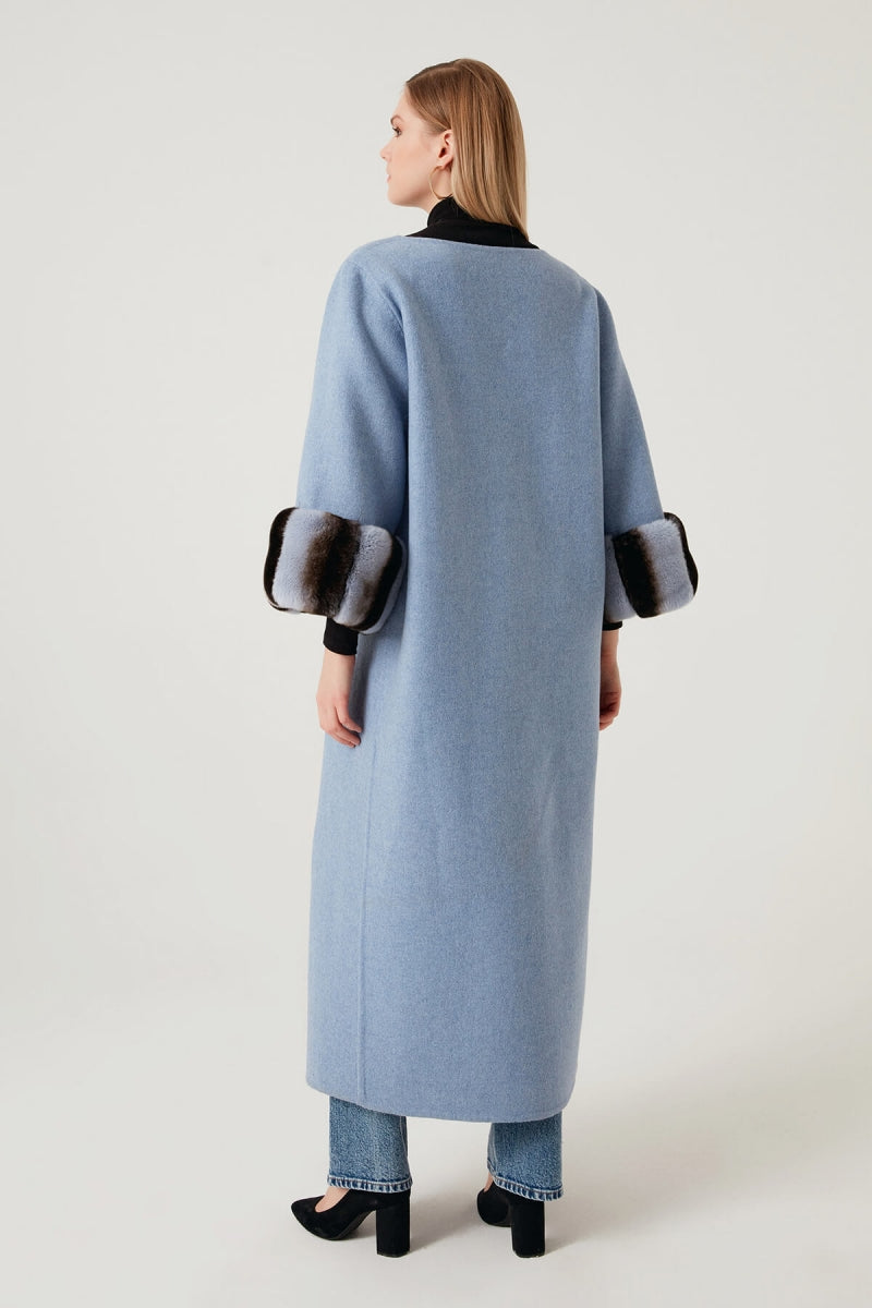 Woman wearing a light blue coat with dark cuffs and collar on a white background