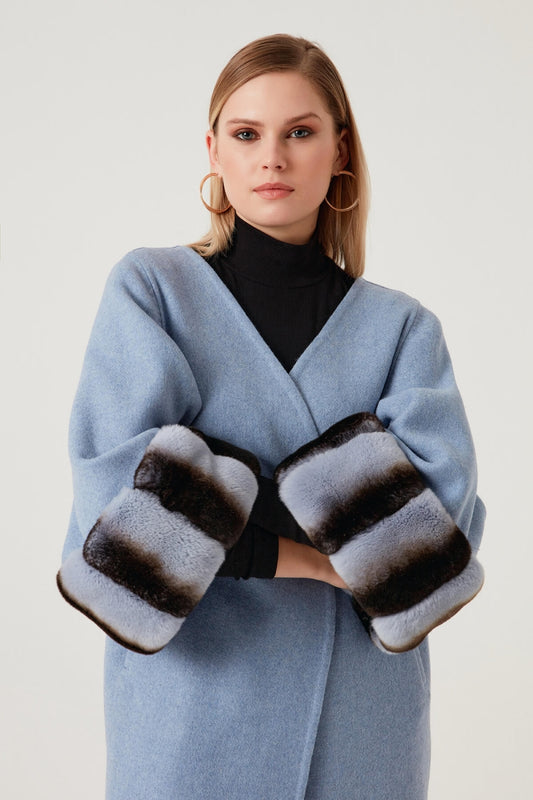 Woman wearing a light blue coat and black gloves with fur trim on a white background