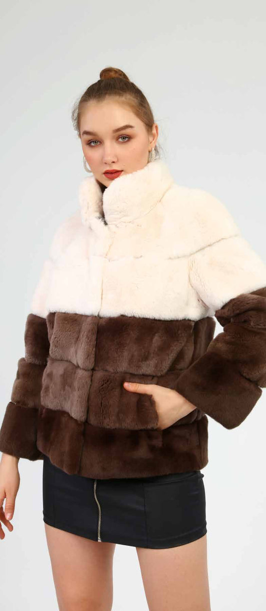 Woman wearing a two-tone fur jacket with white and brown sections on a plain background