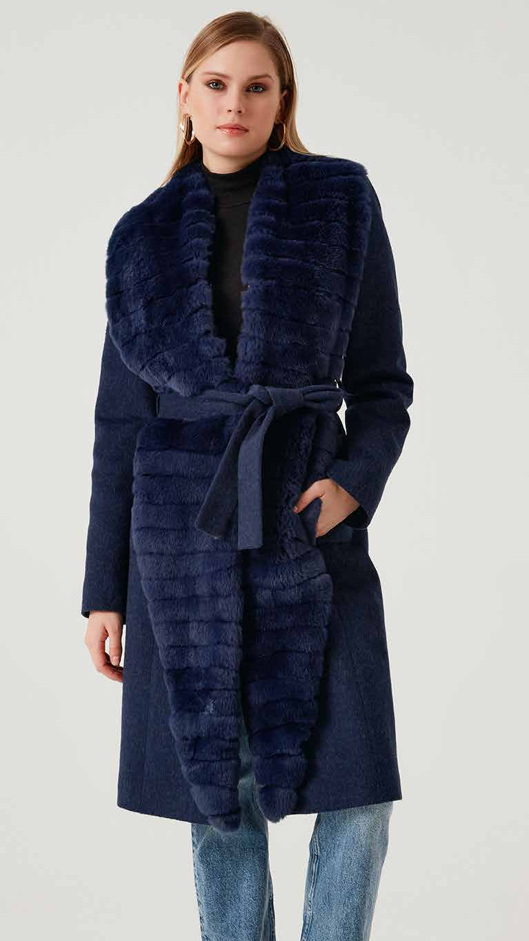 Woman wearing a long navy coat with fur collar on a white background