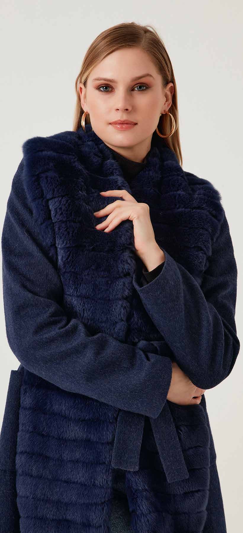 Woman wearing a navy blue coat with fur trim on a white background