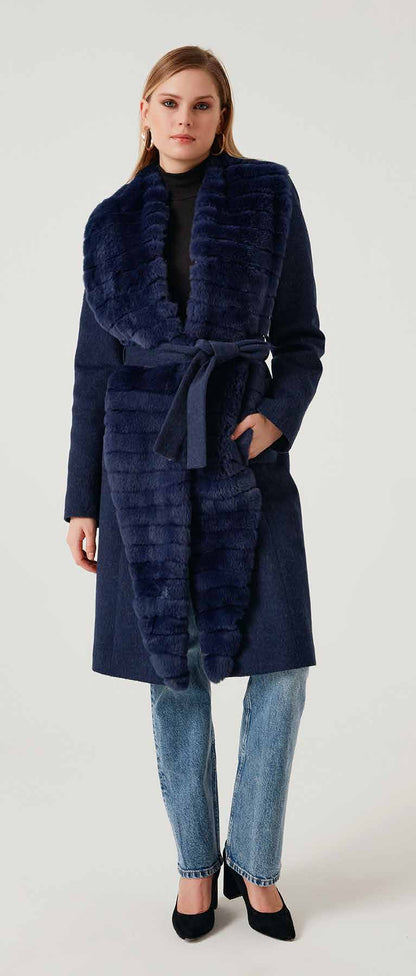 Woman wearing a long navy coat with fur collar on a white background