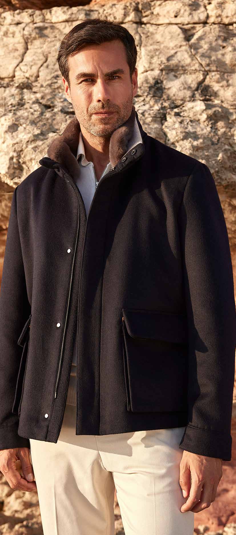 Man wearing a dark coat standing against a stone wall.