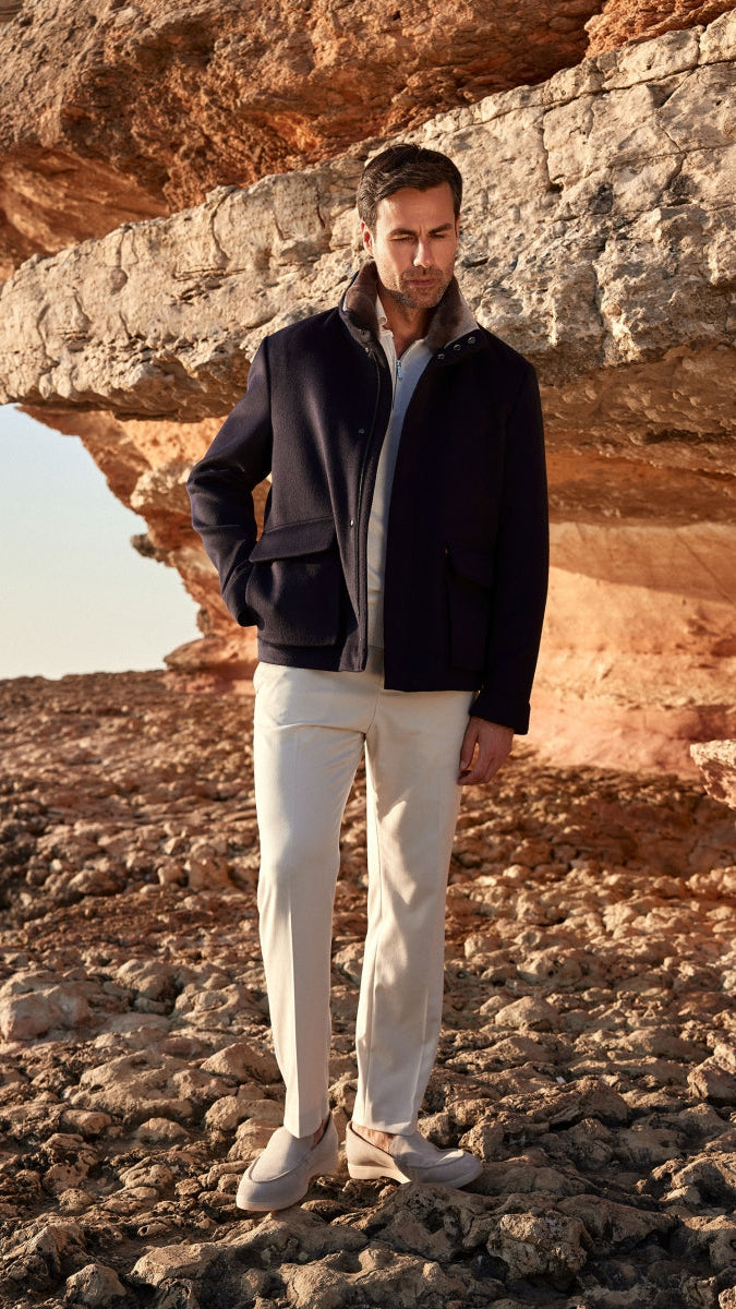 Man standing on rocky terrain wearing a black jacket and white pants.