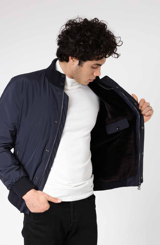 Man wearing a navy bomber jacket over a white turtleneck on a white background