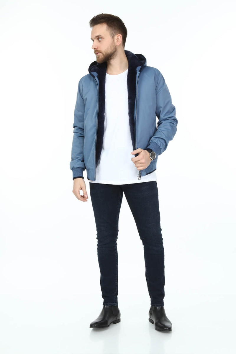 Man wearing a blue jacket with black interior, white shirt, dark jeans, and black shoes on a white background