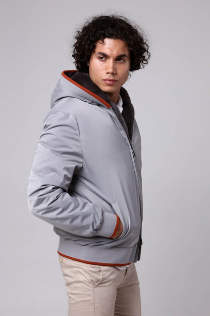 Man wearing a gray jacket with a hood on a plain background