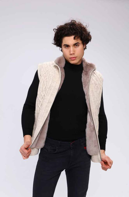 Man wearing a black turtleneck, dark jeans, and a beige quilted vest on a white background
