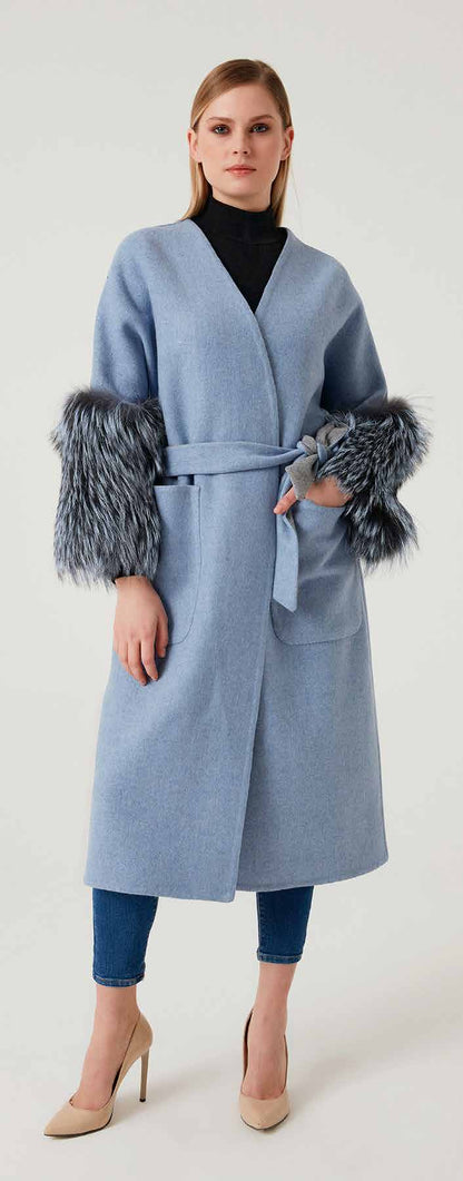 Woman wearing a light blue coat with fur cuffs on a white background