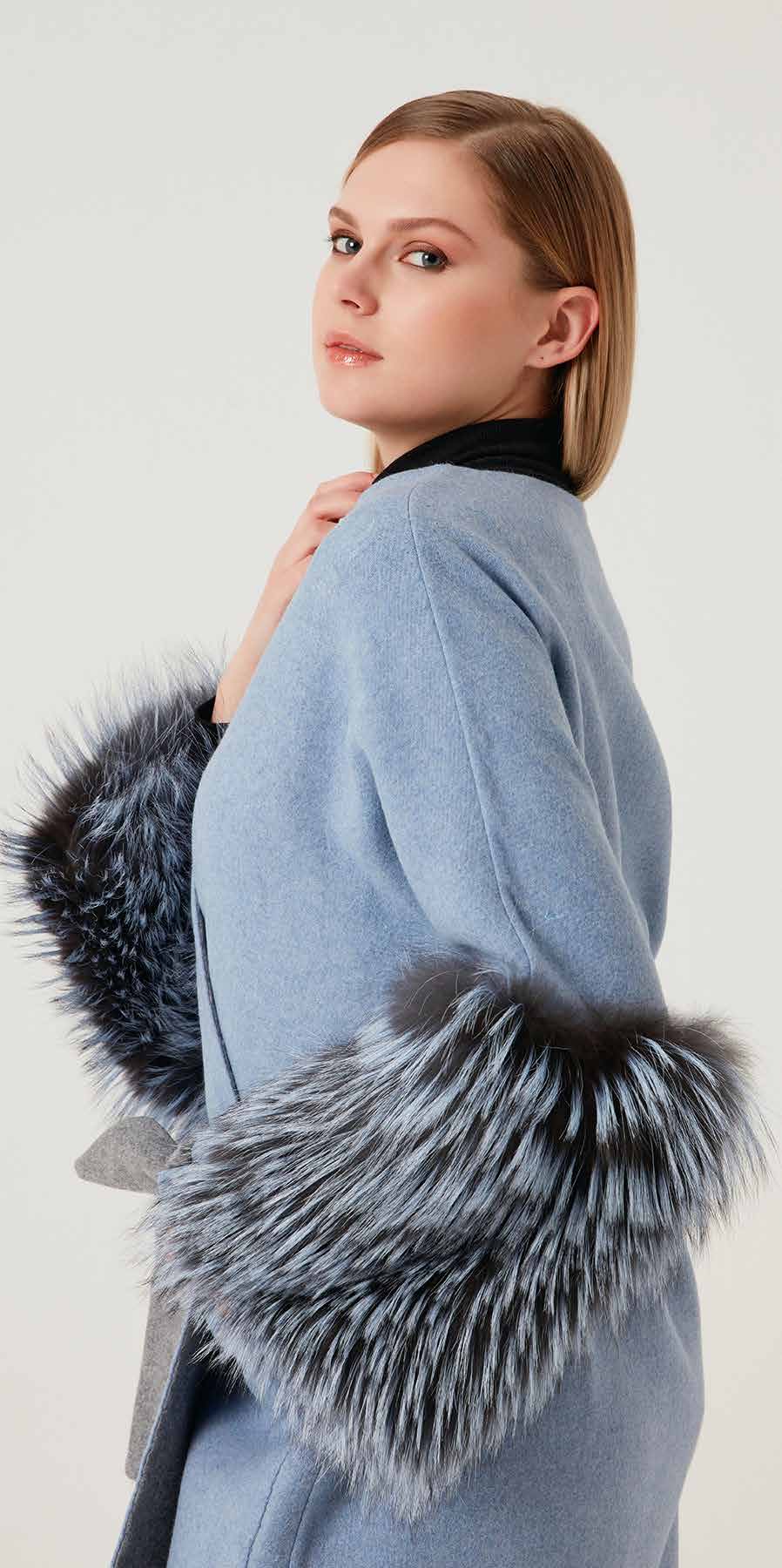 Woman wearing a light blue coat with fur accents on a white background