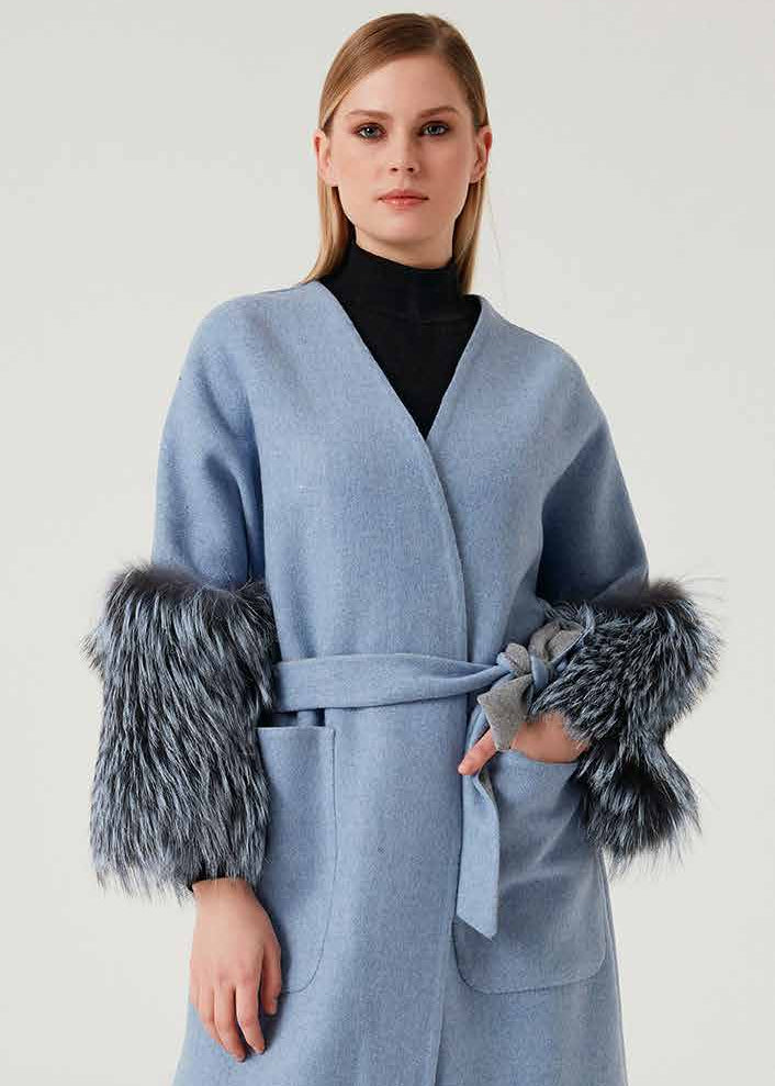 Woman wearing a light blue coat with fur cuffs on a white background