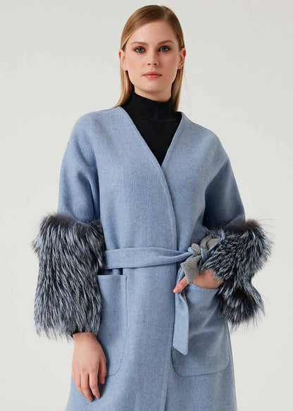 Woman wearing a light blue coat with fur cuffs on a white background