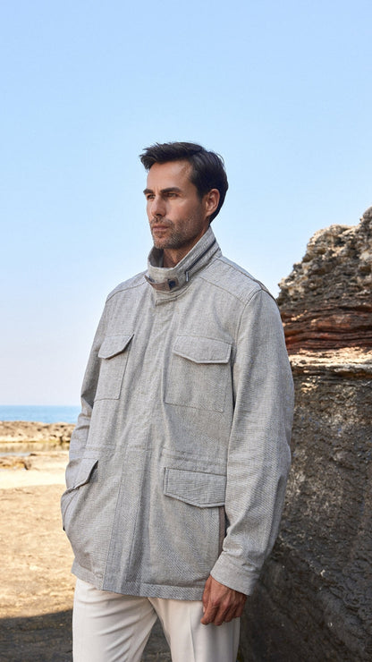 Man wearing a light gray jacket and white pants standing against a rocky coastal background.