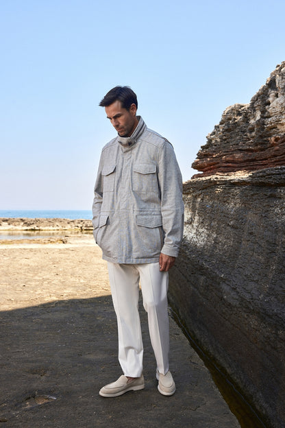Man wearing a gray jacket and white pants standing by a rocky coastal area.