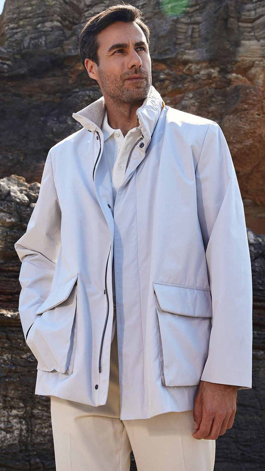 Man wearing a light-colored jacket and pants standing against a rocky cliff background