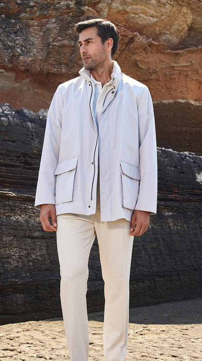 Man in light-colored jacket and pants standing on a rocky beach.