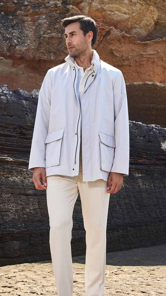 Man in light-colored jacket and pants standing on a rocky beach.