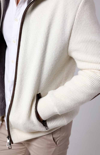 Close-up of a person wearing a white textured jacket with a zipper on a plain background