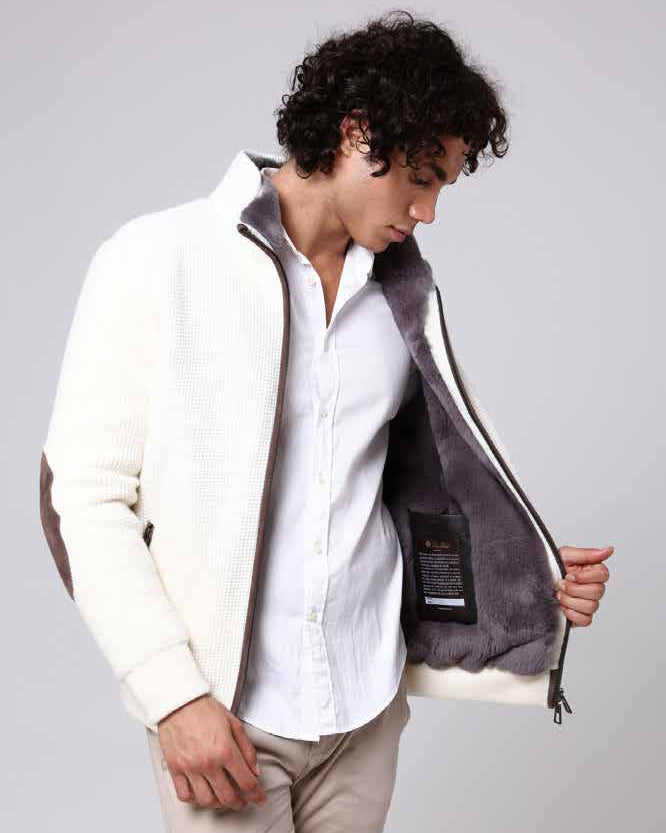 Man wearing a white shirt and beige pants with a gray jacket over his shoulders on a light gray background