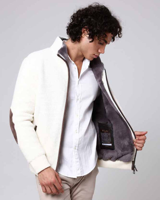 Man wearing a white shirt and beige pants with a gray jacket over his shoulders on a light gray background